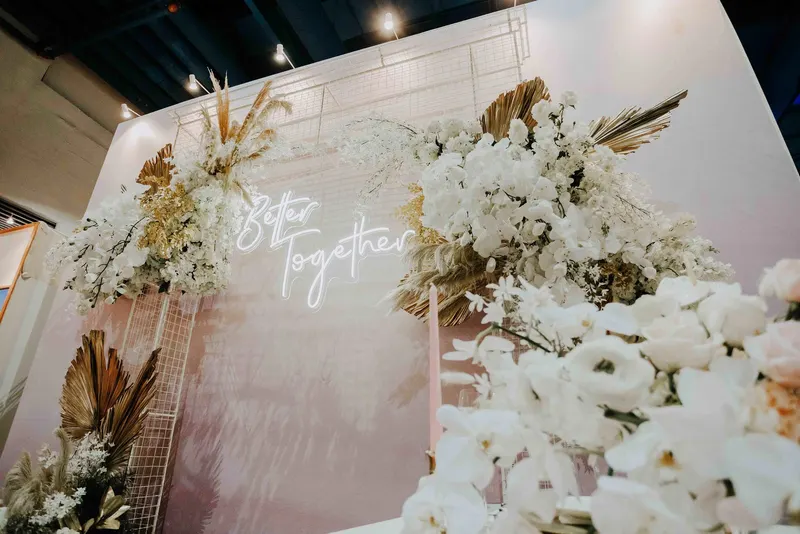 TCE Wedding Expo 'Better Together' neon sign backdrop framed by white flowers and dried palm leaves